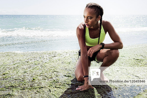 Young woman wearing sports clothing  crouching on beach
