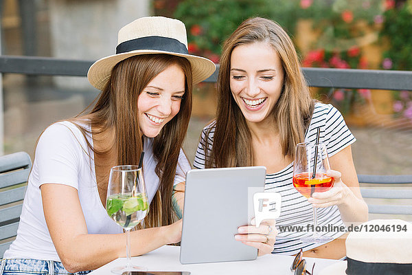 Zwei junge Freundinnen schauen und lachen über das digitale Tablet im Straßencafé