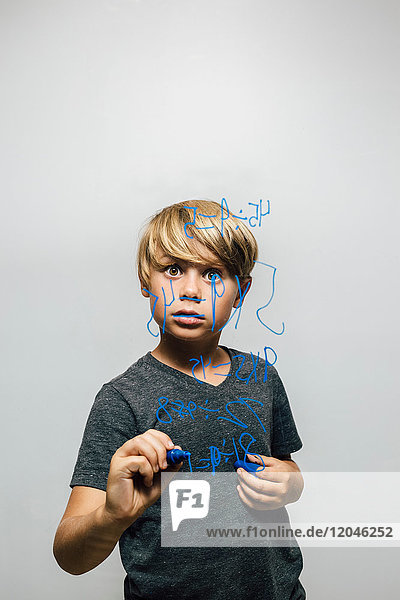 Boy holding blue marker pen staring at equation on glass wall