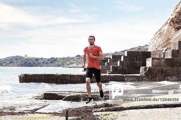 Young male runner running along water's edge of sea defence
