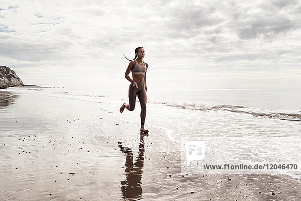 Junge Läuferin läuft am Strand barfuss am Wasser entlang