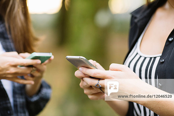 Schnappschuss von zwei jungen Frauen  die den Touchscreen eines Smartphones im Park benutzen