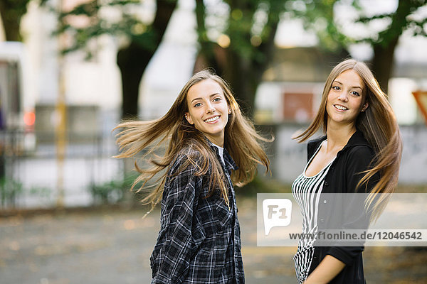 Portrait of two young female friends swirling long brown hair in park
