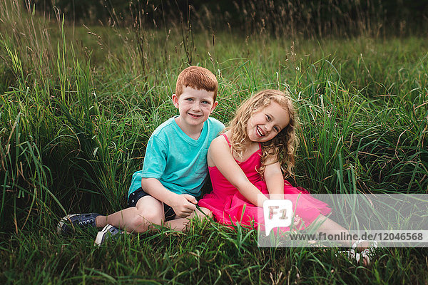 Portrait of girl and brother sitting in field