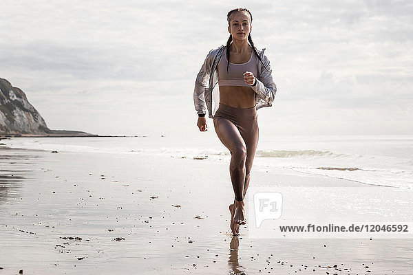 Frontansicht einer jungen Läuferin  die barfuss am Strand entlang läuft