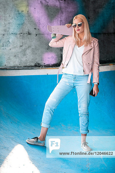 Porträt einer jungen blonden Skateboardfahrerin mit Sonnenbrille auf der Skateboardrampe