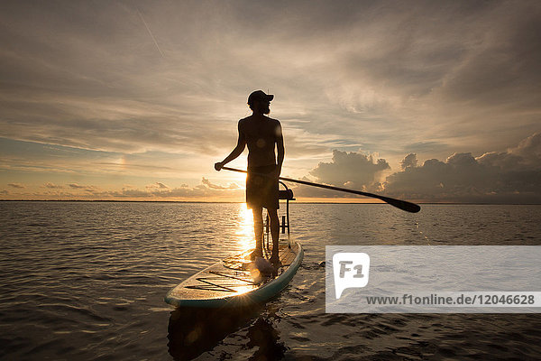 Man standing on paddle board  on water  at sunset