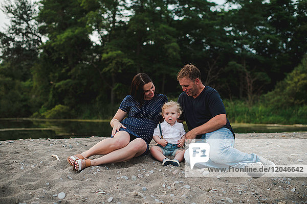 Pregnant couple sitting on beach with male toddler son  Lake Ontario  Canada