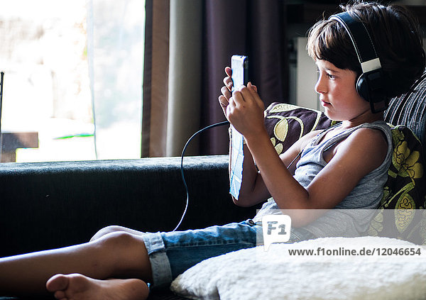 Junge sitzt auf dem Sofa  hört Kopfhörer und starrt auf das digitale Tablet