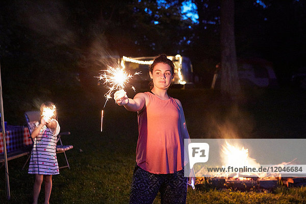 Two girls standing near camp fire  using sparklers