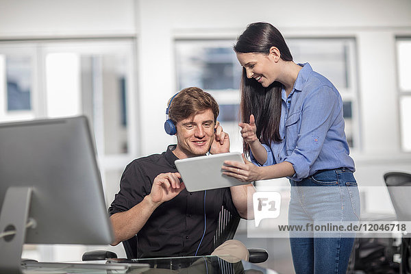 Junge männliche und weibliche Büroangestellte schauen auf digitales Tablet am Büroschreibtisch