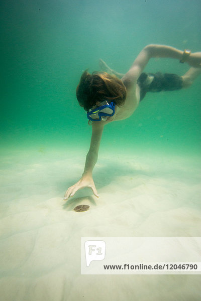 Teenager Junge schwimmt unter Wasser und greift nach Muscheln auf dem Meeresgrund