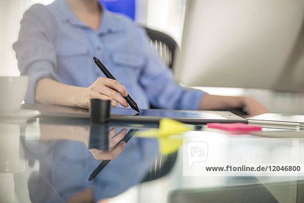 Mittelsektion einer jungen Büroangestellten am Schreibtisch mit digitalem Stift