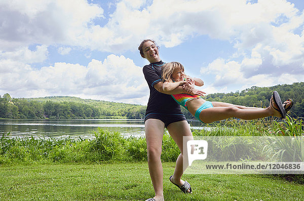 Girl swinging young girl around on grass  beside lake