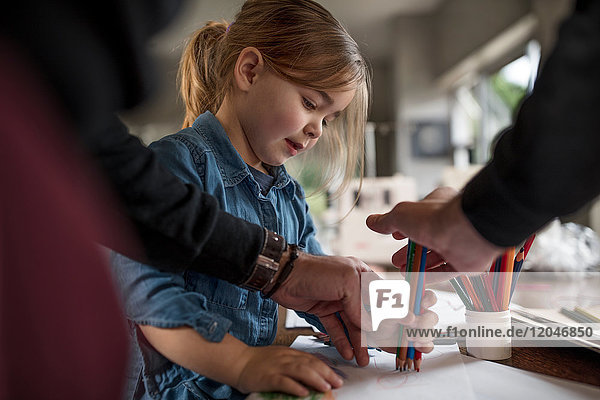 Mann zeigt Tochterzeichnung mit einer Handvoll Farbstiften bei Tisch