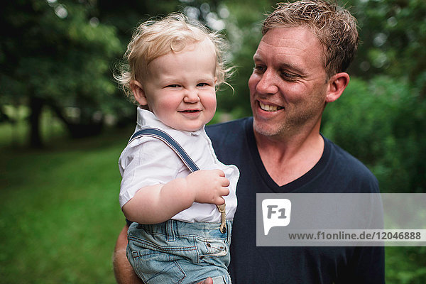 Portrait of man carrying toddler son  pulling a face