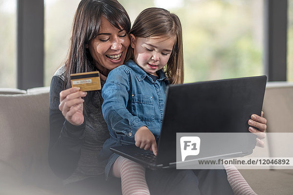 Mädchen und Mutter auf dem Sofa mit Laptop und Kreditkarte beim Online-Shopping