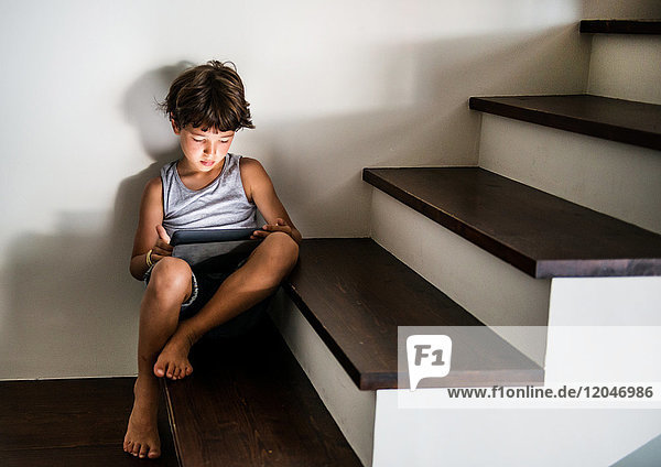Junge sitzt auf einer Treppe und starrt auf ein digitales Tablett