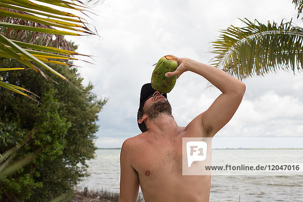 Man beside water drinking from coconut
