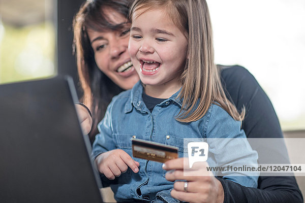 Girl and mother on sofa using laptop and credit card for online shopping