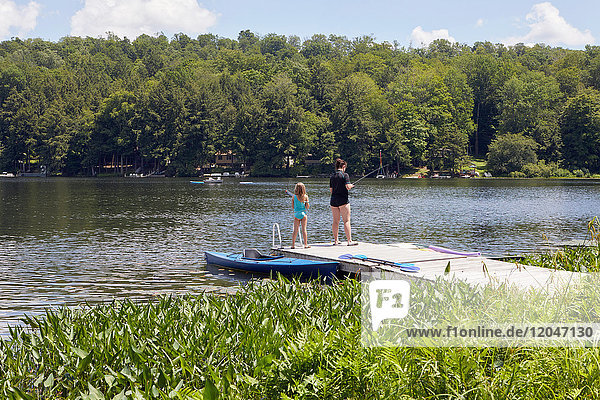 Zwei junge Mädchen stehen auf einem Steg und fischen mit Angelruten