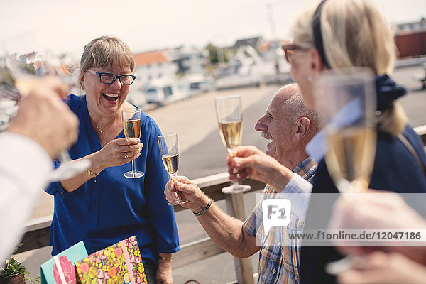 Cheerful senior woman toasting champagne flute with friends on restaurant patio