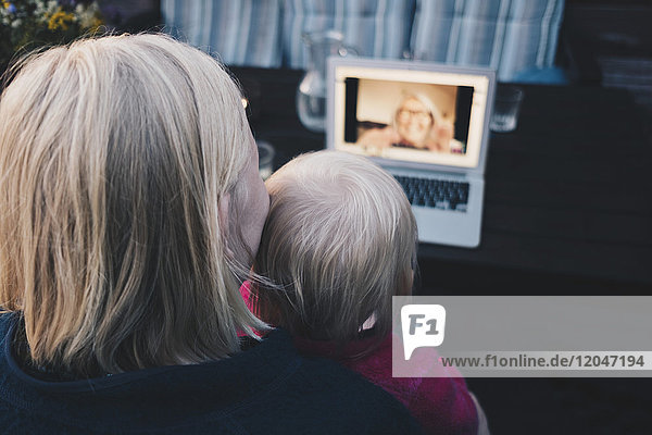 Rückansicht von Mutter und Tochter bei der Videokonferenz am Laptop in der Ferienvilla