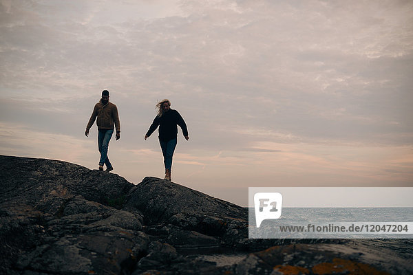 Junger Mann und Frau  die auf einem felsigen Hügel am Strand spazieren gehen.