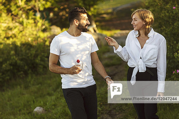 Smiling man and woman talking while walking on grassy field