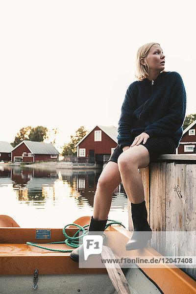 Volle Länge der nachdenklichen Frau die im Boot in der Ferienvilla gegen den klaren Himmel sitzt.