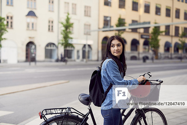 Mittlere erwachsene Frau schaut weg,  während sie mit dem Fahrrad in der Stadt spazieren geht.