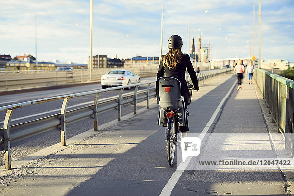 Rear view of businesswoman cycling on bridge against sky