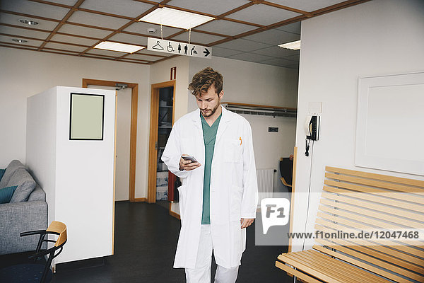 Junger Arzt mit Smartphone beim Gehen im Flur des Krankenhauses
