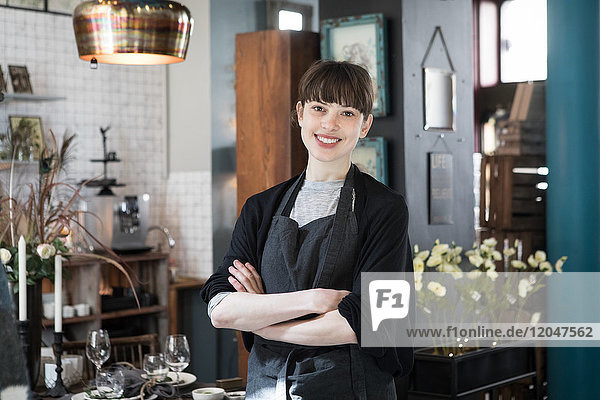 Portrait of smiling young female owner standing with arms crossed at store