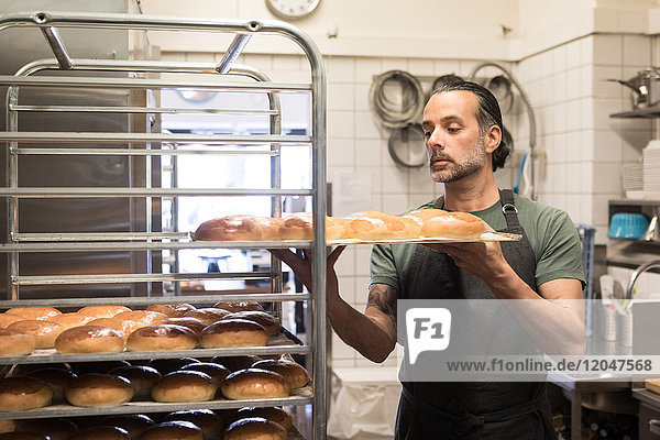 Zuversichtlicher  reifer Mann mit Backblech und frisch gebackenem Brot in der Bäckereiküche.