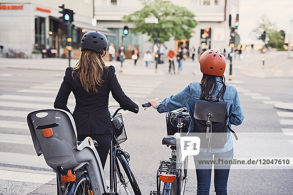 Rückansicht von Frauen mit Fahrrädern,  die die Straße in der Stadt überqueren.