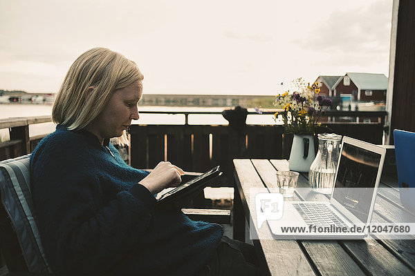 Frau mit digitalem Tablett und Laptop auf Holztisch in der Ferienvilla