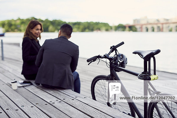 Business colleagues sitting by bicycle at pier