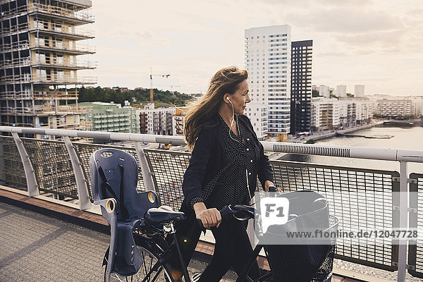 Reife Frau  die mit dem Fahrrad auf einer Fußgängerbrücke in der Stadt spazieren geht.