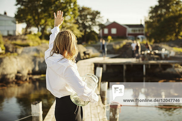 Rear view of young woman waving to friends standing on jetty at harbor