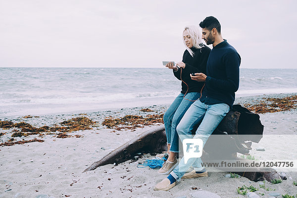Volle Länge des jungen Mannes und der Frau beim Sitzen auf Metall am Strand.