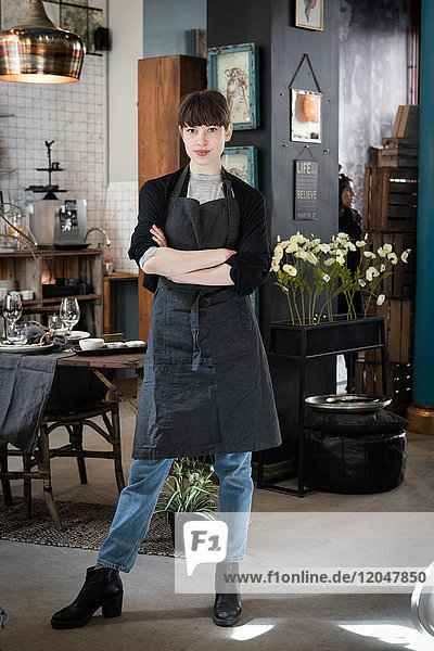 Full length portrait of confident young female owner standing with arms crossed at store