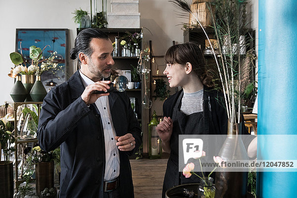 Smiling young female entrepreneur talking with mature male customer holding magnifying glass at store