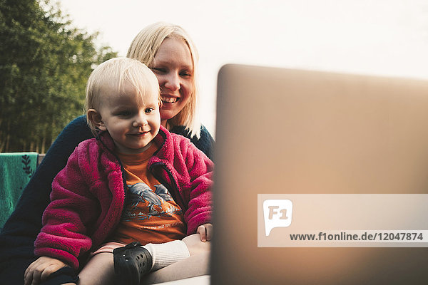 Lächelnde Mutter und Tochter beim Blick auf den Laptop während der Videokonferenz an einem sonnigen Tag