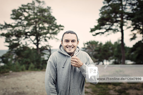 Portrait of smiling young man zipping hooded sweatshirt in back yard