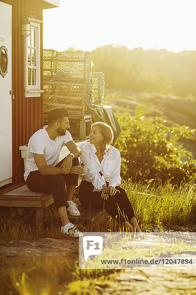 Young couple talking while sitting at log cabin on sunny day