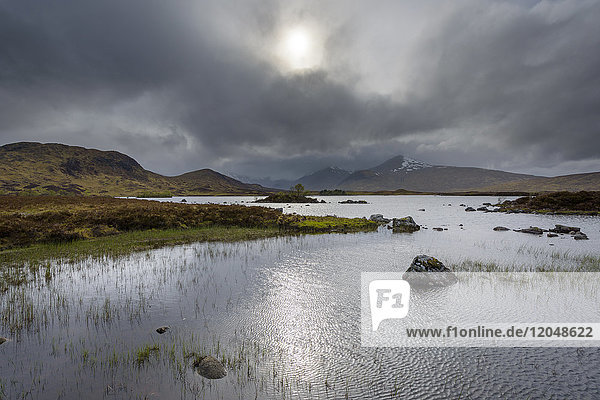 Moor landscape with a river and the sun glowing through dense cloudy sky at Rannoch Moor in Scotland  United Kingdom