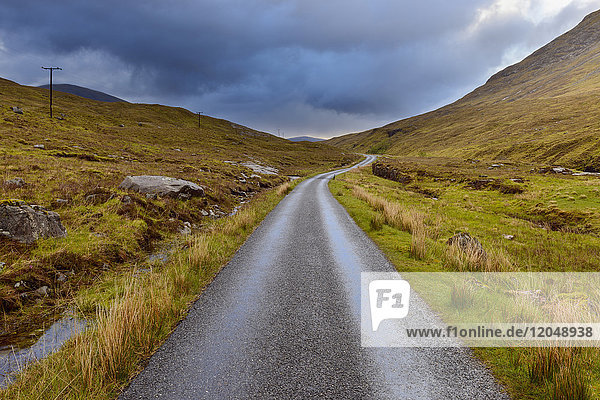 Kurvenreiche Straße in den Highlands mit bewölktem Himmel in Glen Coe in Schottland  Vereinigtes Königreich