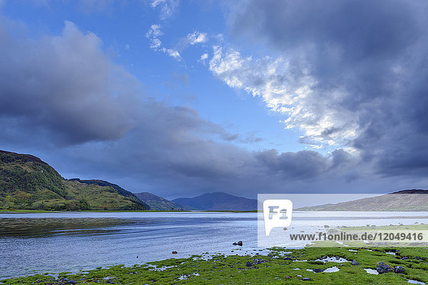 Grassy shoreline with dramatic clouds at sunrise along Scottish coast near Eilean Donan Castle and Kyle of Lochalsh in Scotland