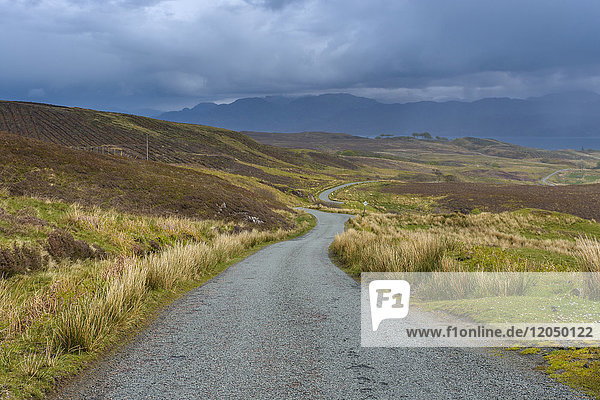 Kurvenreiche einspurige Straße durch die Landschaft bei bedecktem Himmel im Frühling auf der Isle of Skye in Schottland  Vereinigtes Königreich